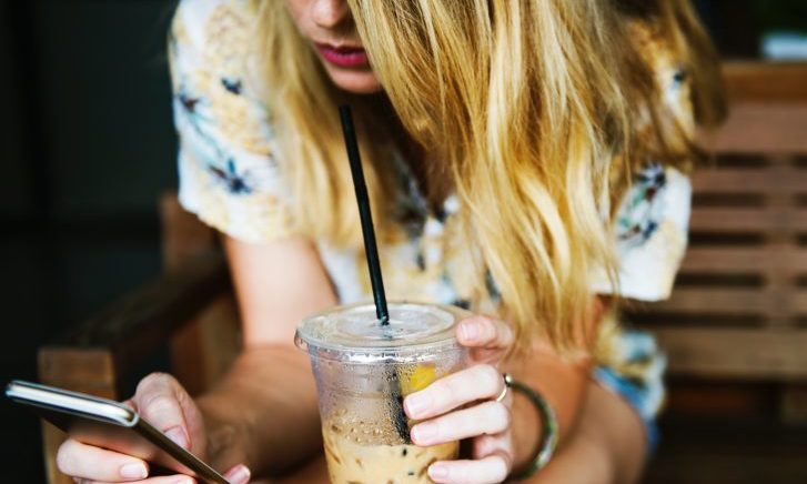 左手にカフェラテを持ってスマホをいじっている外国人女性